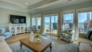 A spacious living room with a wooden coffee table, a white console, and a large TV. - Flamingo Villa - Oceanfront B Luxury Home, Hot Tub, 6 bed 4.5 bath (North Topsail Beach)