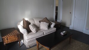 A living room with a beige sofa, two pillows, a small wooden side table, and a black coffee table. - Light House  , Unique Apartment in the Heart of the city  (Winnipeg)