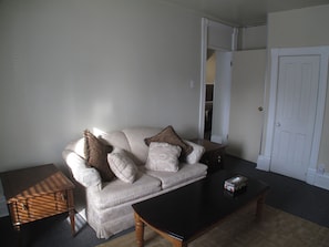 A living room with a beige sofa, two pillows, a small wooden side table, and a black coffee table.