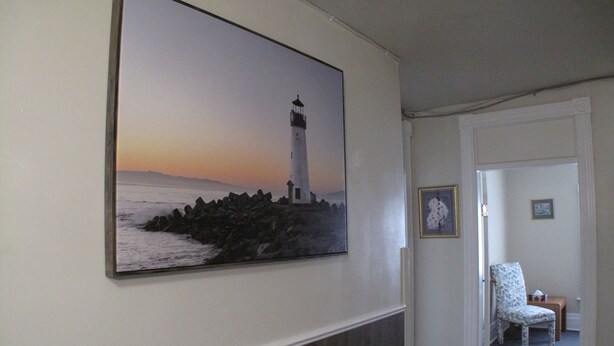 A hallway with a framed painting of a lighthouse, a patterned chair, and a door leading to another room. - Light House  , Unique Apartment in the Heart of the city  (Winnipeg)