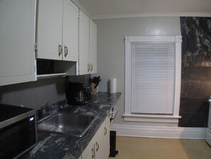 A kitchen with white cabinets, a black countertop, a sink, a coffee maker, and a window with blinds.