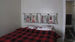 A bedroom with a bed, a red and black checkered bedspread, and a wall with four nautical-themed curtains. - Light House  , Unique Apartment in the Heart of the city  (Winnipeg)