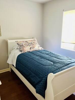 A single-bed room with a white frame, a patterned blue quilt, and a white pillow.