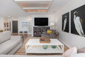 A modern living room with a flat-screen TV, a sofa, a coffee table, and artwork on the walls.
