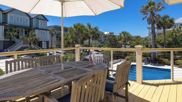 A wooden deck with a pool, outdoor furniture, and a view of a residential area with palm trees and houses. - Spacious 4-Bedroom Beach House with Pool and Ocean Views (Isle Of Palms)
