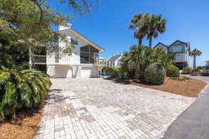 A residential property with a paved driveway, a pool, and a well-maintained garden with palm trees.