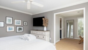 A bedroom with a large bed, a dresser, a flat-screen TV, and framed artwork on the wall. - Spacious 4-Bedroom Beach House with Pool and Ocean Views (Isle Of Palms)