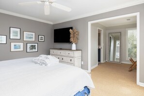 A bedroom with a large bed, a dresser, a flat-screen TV, and framed artwork on the wall. - Spacious 4-Bedroom Beach House with Pool and Ocean Views (Isle Of Palms)