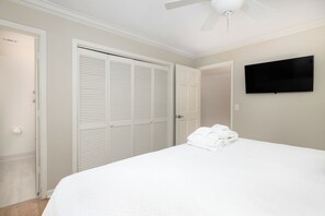 A bedroom with a bed, a closet, a television, and a ceiling fan.