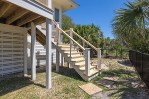 A staircase leading to a house with a covered porch, surrounded by palm trees and a fence.