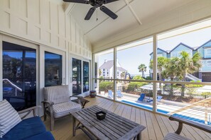 Área externa coberta com piscina, espreguiçadeiras e vista para o oceano e casas vizinhas.