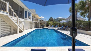 A swimming pool with a clear blue water, surrounded by lounge chairs and umbrellas, and a staircase leading to a second floor. - Spacious 4-Bedroom Beach House with Pool and Ocean Views (Isle Of Palms)