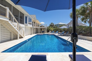 A swimming pool with a clear blue water, surrounded by lounge chairs and umbrellas, and a staircase leading to a second floor. - Spacious 4-Bedroom Beach House with Pool and Ocean Views (Isle Of Palms)