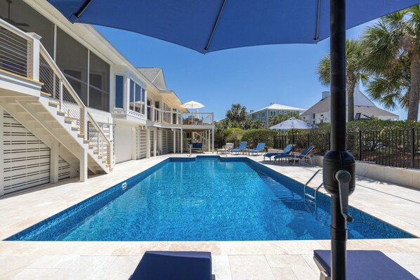 A swimming pool with a clear blue water, surrounded by lounge chairs and umbrellas, and a staircase leading to a second floor.