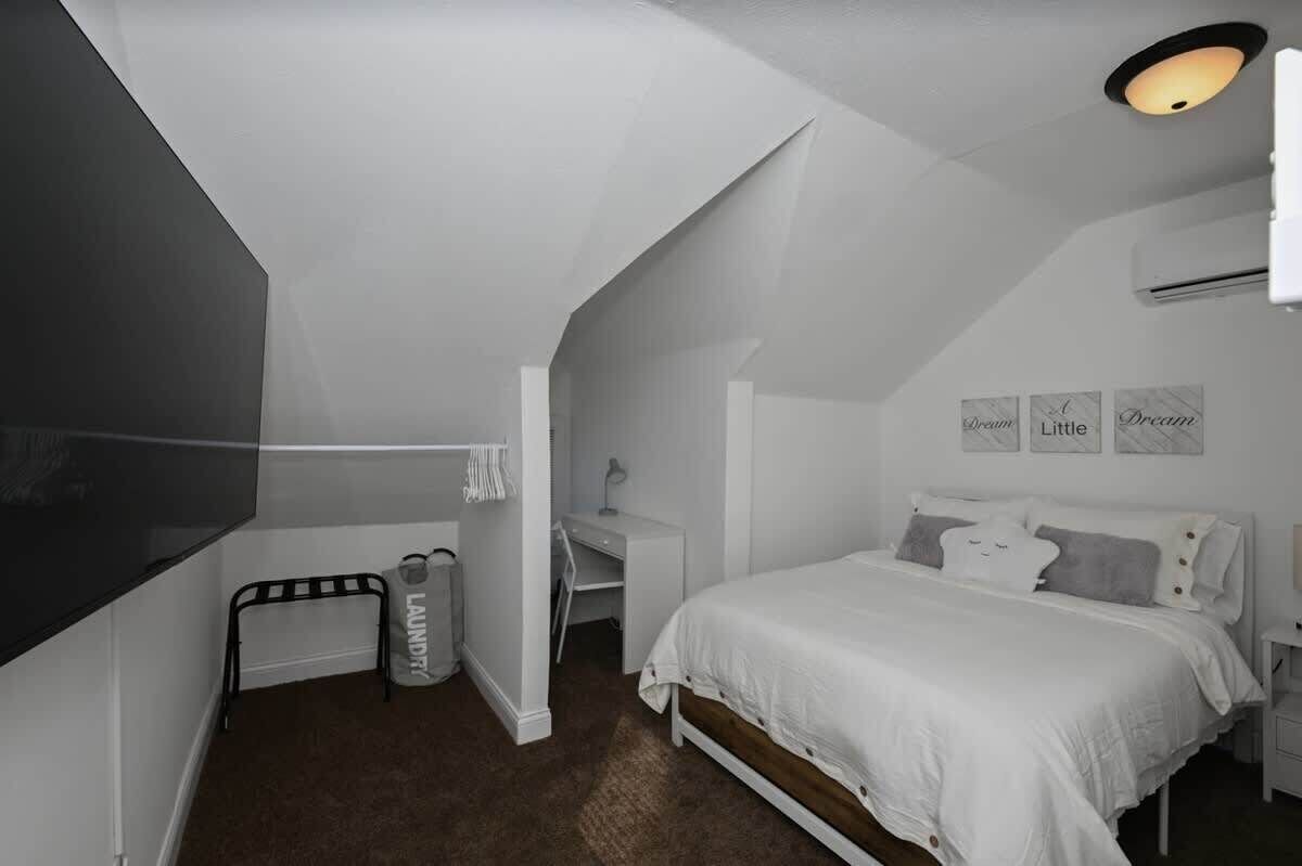 A bedroom with a sloped ceiling, a bed, a desk, and a chair.