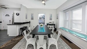 Una cocina moderna con comedor, sillas blancas, una mesa negra y un ventilador de techo.