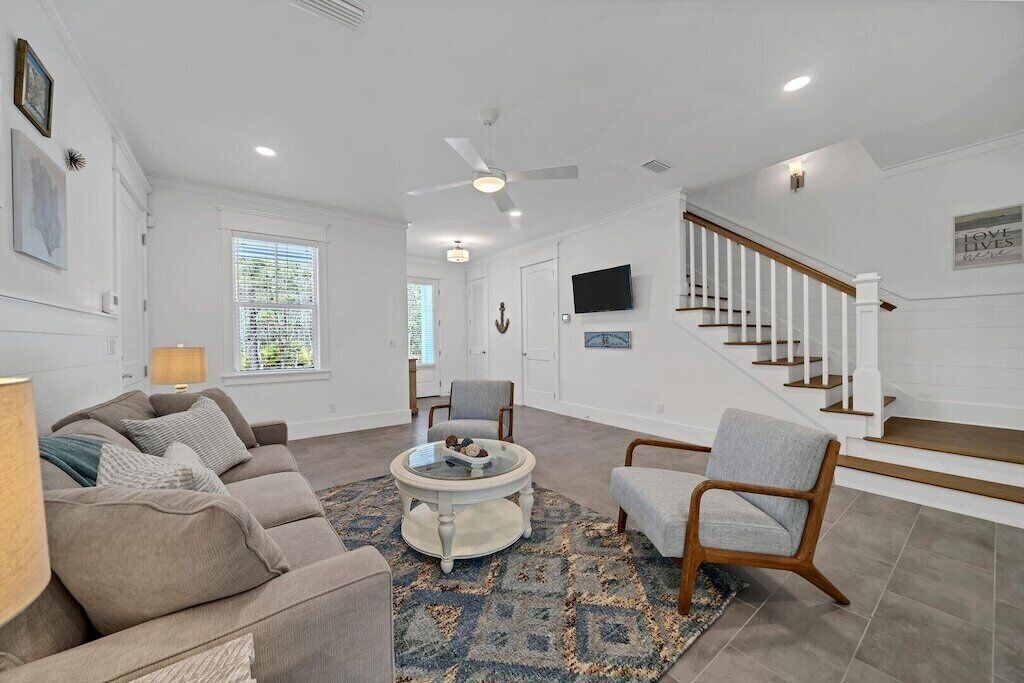 A spacious living room with a beige sofa, a round coffee table, and a staircase with white railings.