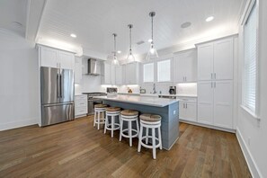 Una cocina moderna con armarios blancos, un refrigerador de acero inoxidable, una isla central con taburetes e iluminación colgante.