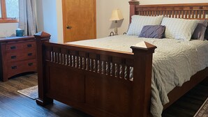 A bedroom with a wooden bed, a nightstand, a lamp, a window with curtains, and a door. -  Home on Quiet Cul de Sac with Handicap Accessibility (Kearney)