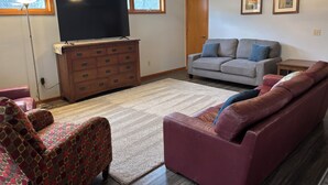 A living room with a television, a wooden dresser, a gray sofa, a red patterned chair, and a ceiling fan. -  Home on Quiet Cul de Sac with Handicap Accessibility (Kearney)
