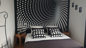 Un dormitorio con cabecera a lunares blancos y negros, dos mesitas de noche y una cama con almohadas a juego.