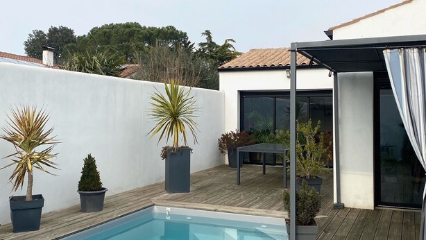 Una piscina con cubierta de madera, rodeada de plantas en macetas y un área de estar techada.