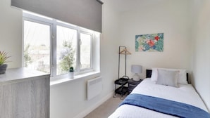 A bedroom with a bed, bedside table, lamp, and a window with a view of trees. - Beautiful 2-bed Apartment in Tunbridge Wells (Royal Tunbridge Wells)