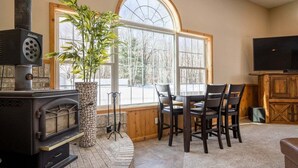 A cozy living room with a fireplace, a dining area, and a television. - Private 5-Acre Estate | Fishing Pond + Fire Pit (West Olive)
