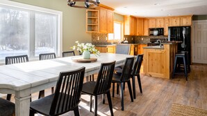 A spacious kitchen with wooden cabinets, a large island, and a dining area with chairs. - Private 5-Acre Estate | Fishing Pond + Fire Pit (West Olive)