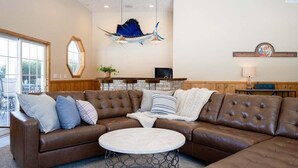 A living room with a brown leather sectional sofa, a round coffee table, and a hanging blue sailboat decoration. - Private 5-Acre Estate | Fishing Pond + Fire Pit (West Olive)