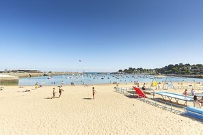 Een strand met een zandstrand, een zwembad en een speeltuin met glijbanen en schommels.