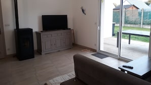 Een woonkamer met een bank, een televisie op een kast, een open haard en een schuifpui naar een terras.