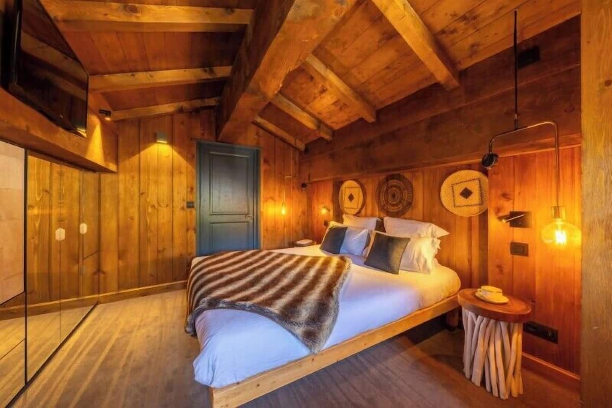 Ein schlicht eingerichtetes Schlafzimmer im Chalet-Stil mit einem Bett, Nachttischen und Wandleuchten.