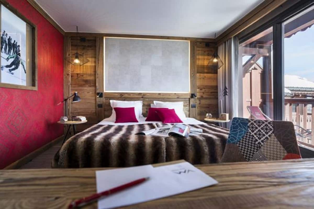 Ein Hotelzimmer mit einem großen Bett, Holzwänden, einem Balkon mit Bergblick und einem großen Fenster.