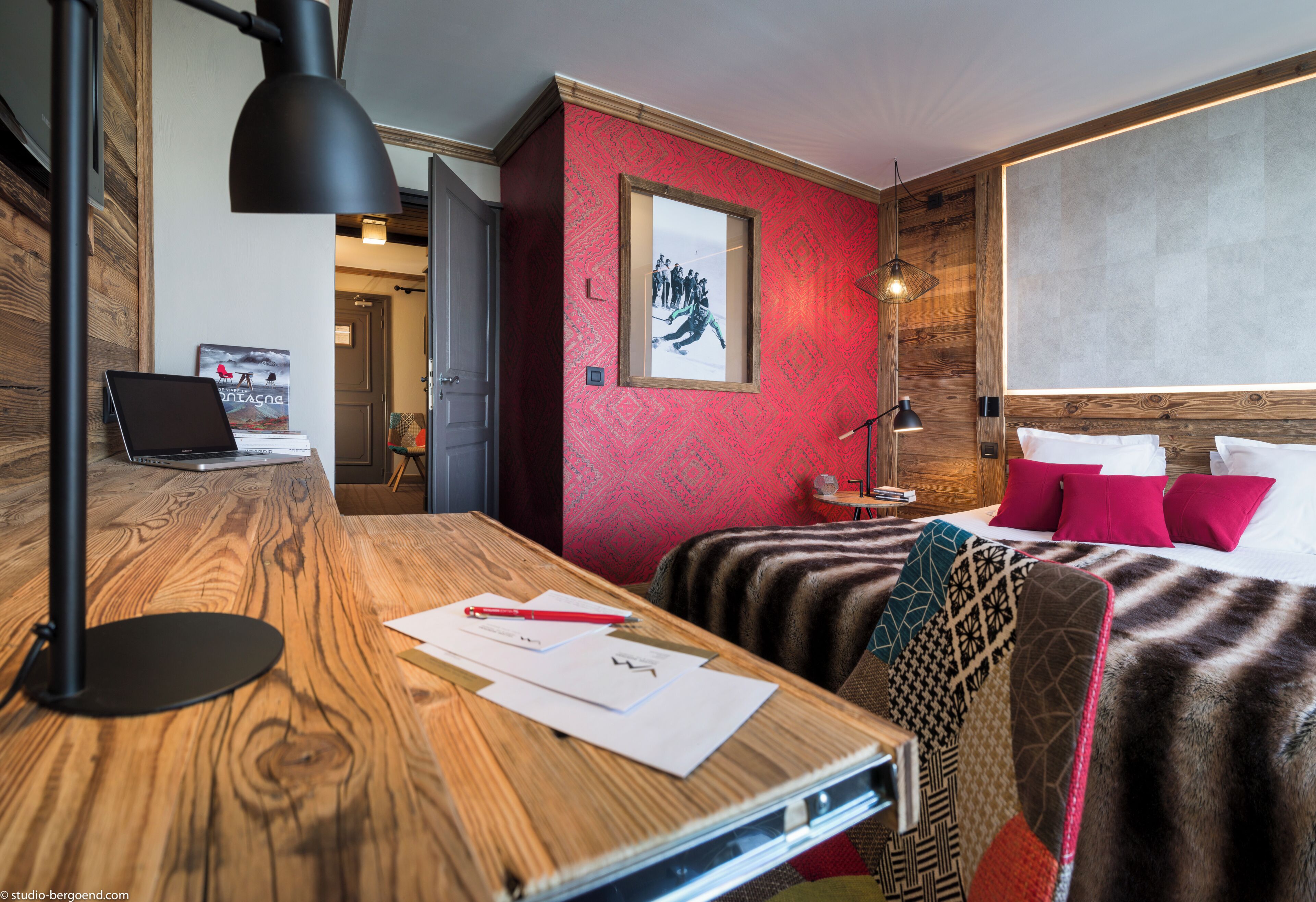 A hotel room with a wooden desk, a laptop, a bed with patterned bedding, and a framed picture on the wall.