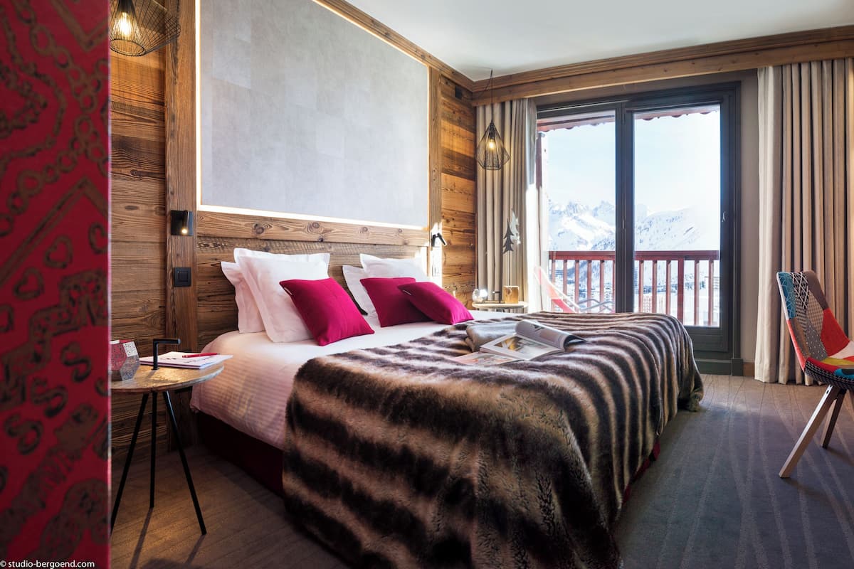 Ein Hotelzimmer mit Bett, Schreibtisch, Laptop, Stuhl und Blick auf Berge durch das Fenster.
