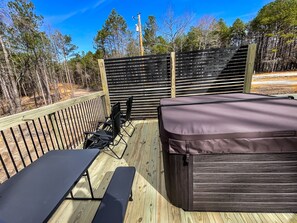 A wooden deck with a hot tub, two fold-out chairs, and a picnic table.