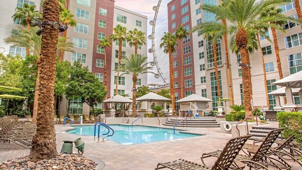 A hotel pool area with palm trees, lounge chairs, and a Ferris wheel in the background. - 2 BR/2 BA with Kitchen at Hilton HGVC (Las Vegas)