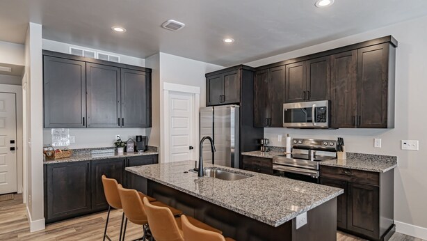 A modern kitchen with dark wood cabinets, granite countertops, stainless steel appliances, and a central island with bar stools.