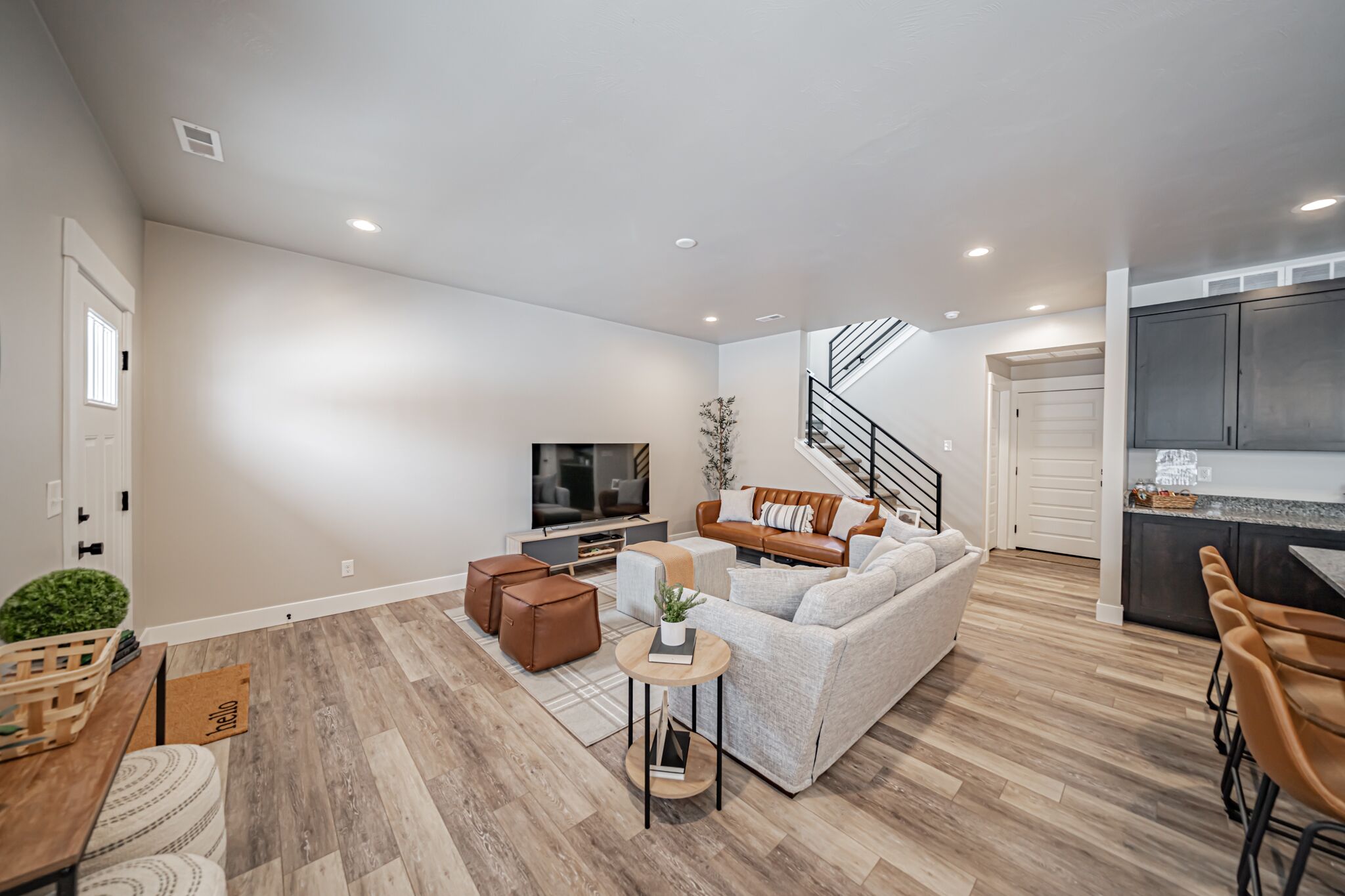 A modern living room with a sofa, coffee table, and TV. There is a staircase leading to a kitchen area.