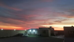 Una azotea con vista al atardecer, que incluye un edificio pequeño con techo plano y algunas luces.