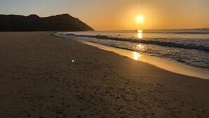 Una playa con un atardecer, olas tranquilas y una montaña distante.