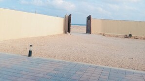 Un sendero pavimentado que conduce a una playa, con cielo despejado y dos grandes puertas de madera.