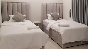 Habitación de hotel con dos camas, cada una con cabecera, mesita de noche y cortina.