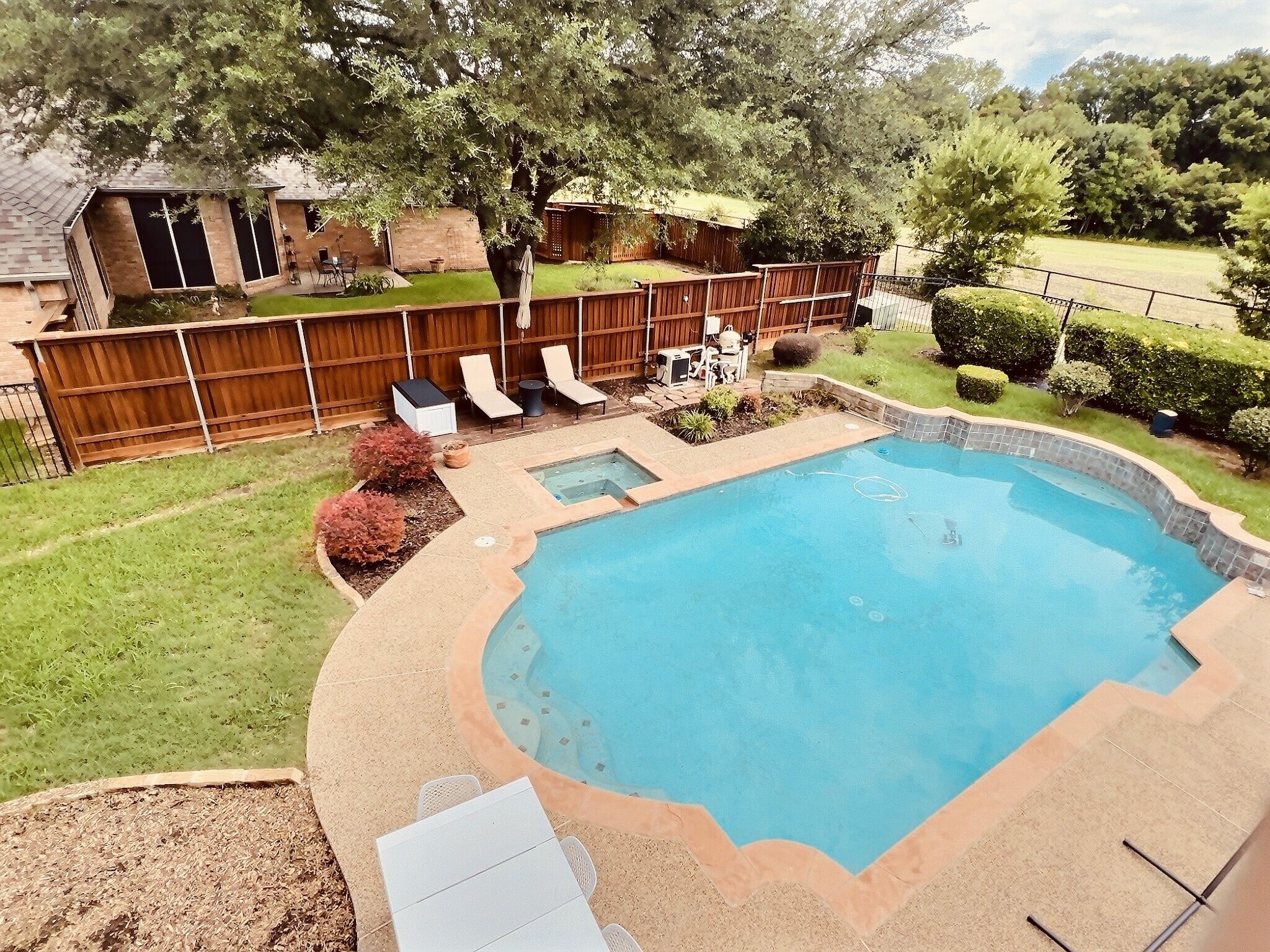 A backyard with a swimming pool, a wooden deck, and a fenced area with outdoor furniture.
