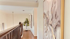 A hallway with wooden flooring, a railing, and a large abstract painting on the wall.