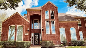 A two-story brick house with a central entrance, large windows, and a well-maintained lawn.