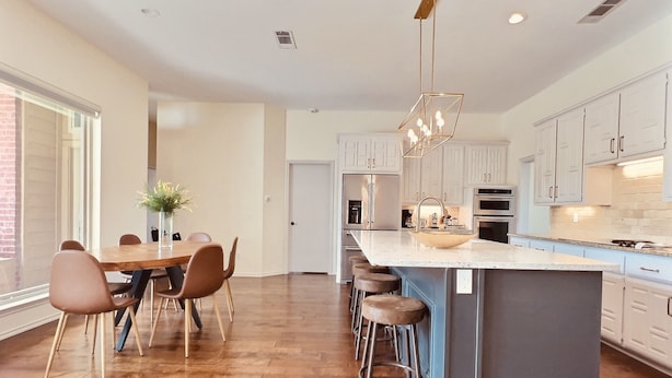 A modern kitchen with a large island, bar stools, and a dining area with a wooden table and chairs.