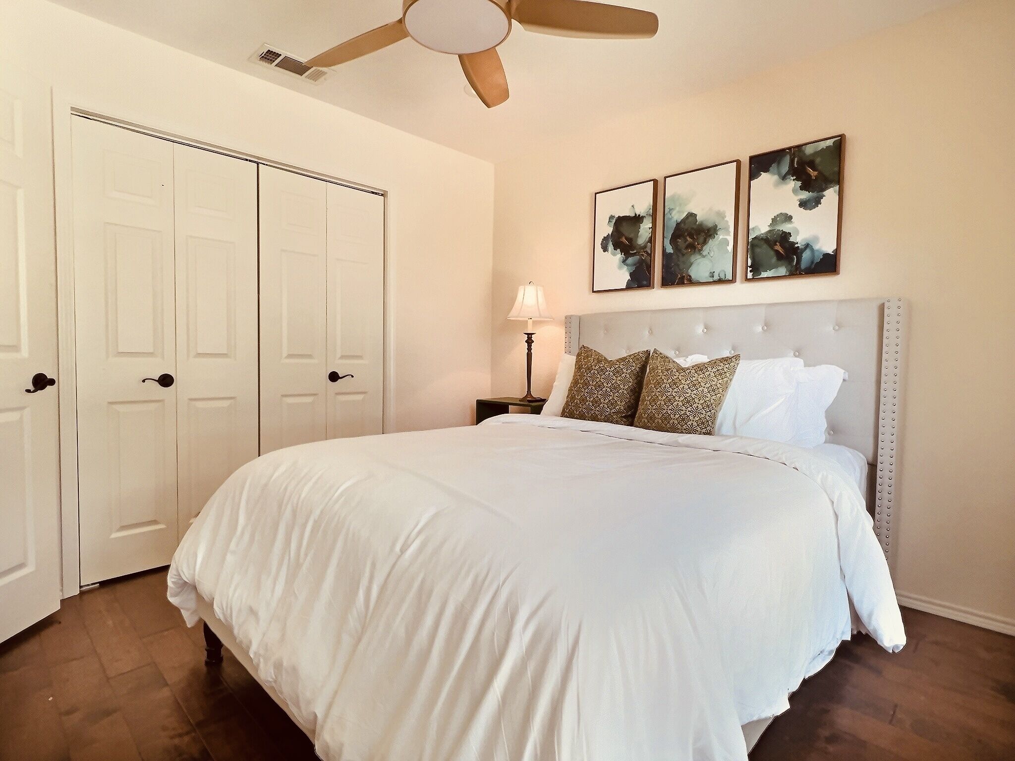 A bedroom with a large bed, a ceiling fan, and three framed artworks on the wall.