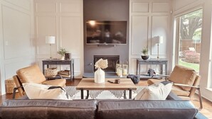 A modern living room with a fireplace, leather sofas, a coffee table, and a large TV.